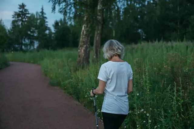 Vanhempi nainen kävelee sauvoilla puiston polulla
