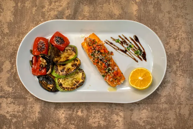 Lautasella grillattua lohta, paahdettuja kasviksia ja sitruunaa
