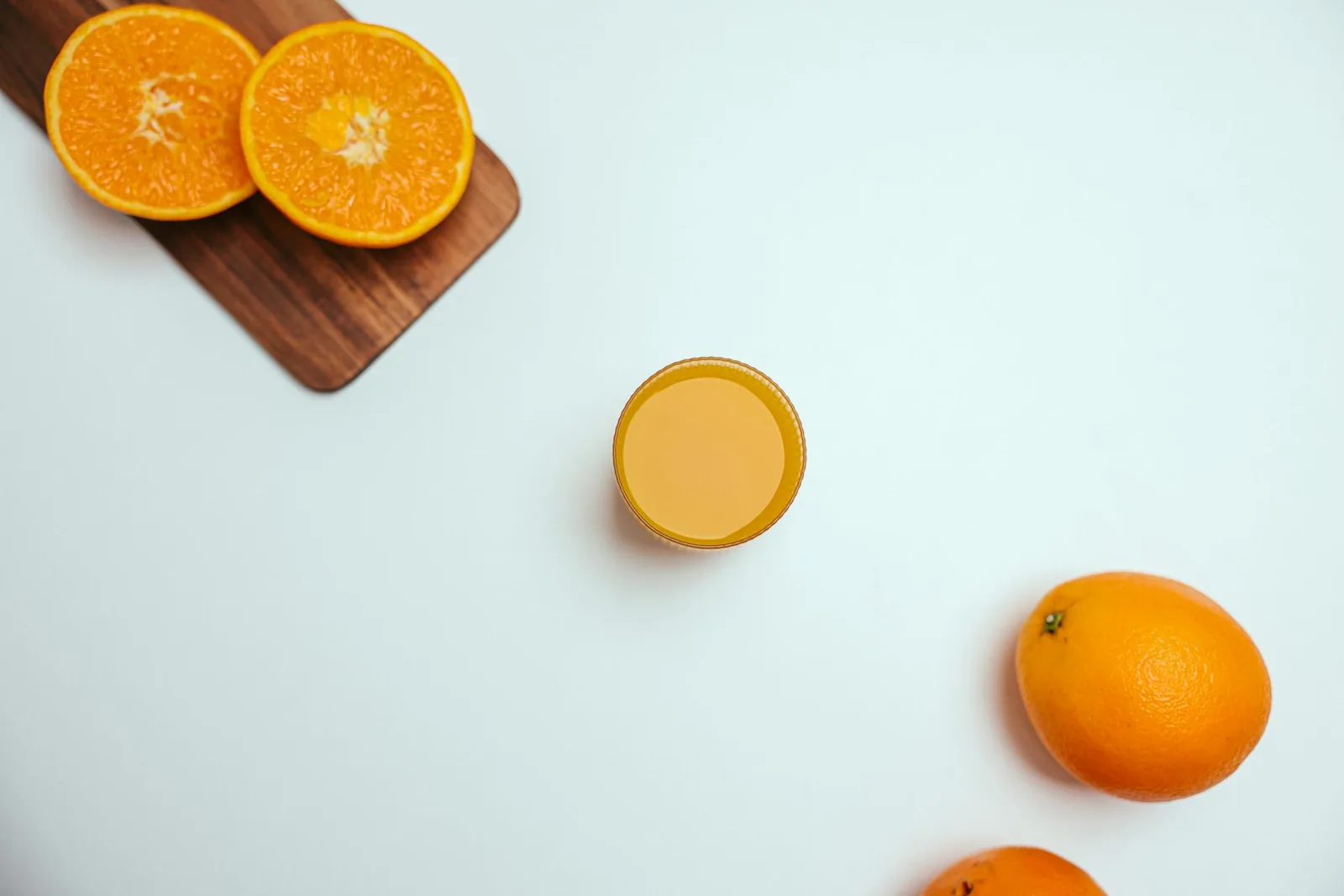 Appelsiineja, appelsiininpuolikkaita ja lasillinen tuoremehua vaalealla pinnalla