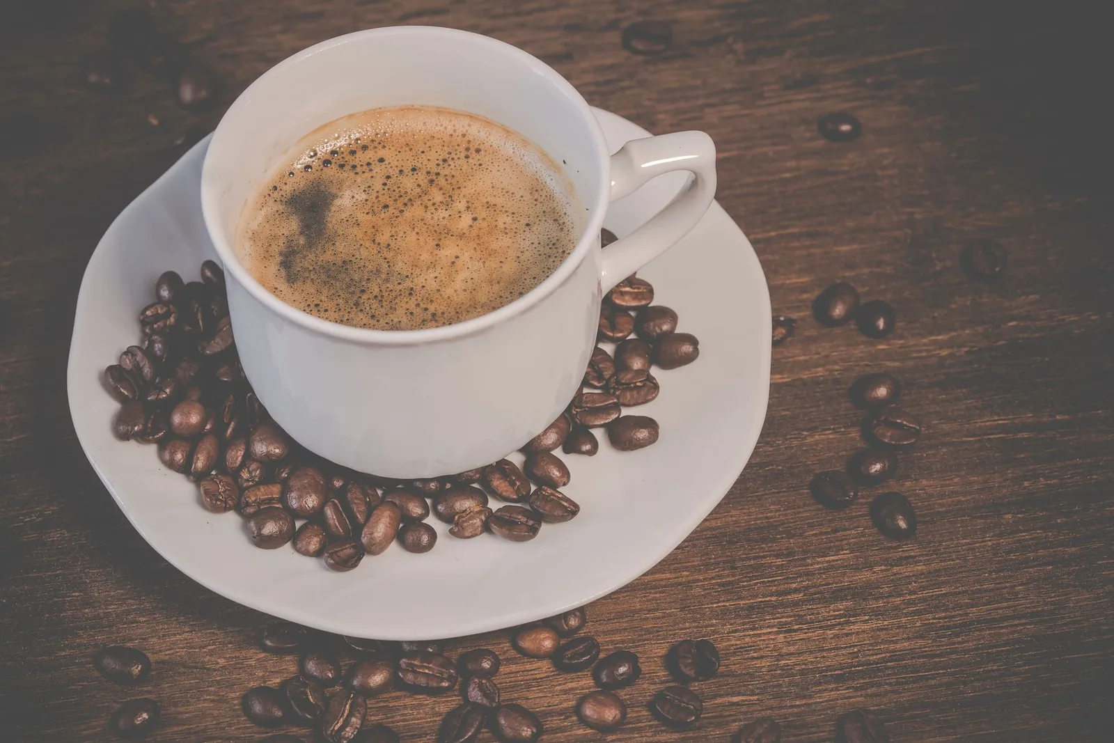 Espressokuppi ja kahvipapuja puupöydällä